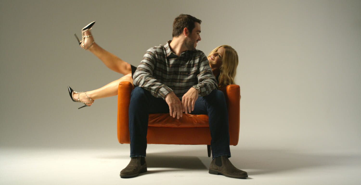 man and woman seated on orange chair looking at each other in studio space
