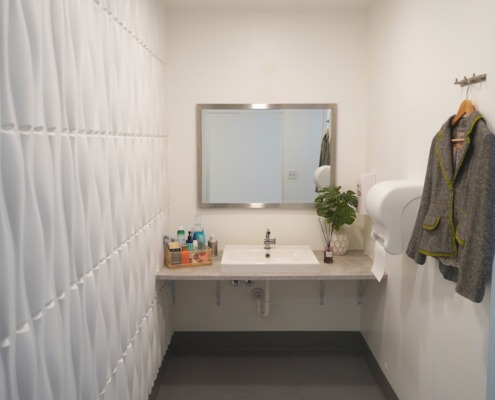 Clean modern bathroom with clothing hooks and basket of amenities on counter