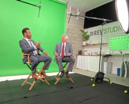 Two men in directors chairs in front of green screen on set